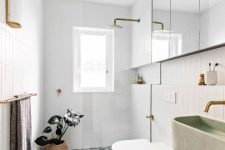 a small mid-century modern bathroom with white skinny and geo blue and white tiles, a shower space, a mirror cabinet, a green sink and gold fixtures