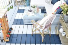 a small striped deck with rattan furniture, an L-shaped bench with pillows, potted greenery and a blue coffee table