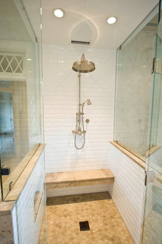 a smll shower space with white tiles, a floating earthy bench and a matching floor plus glass walls on two sides