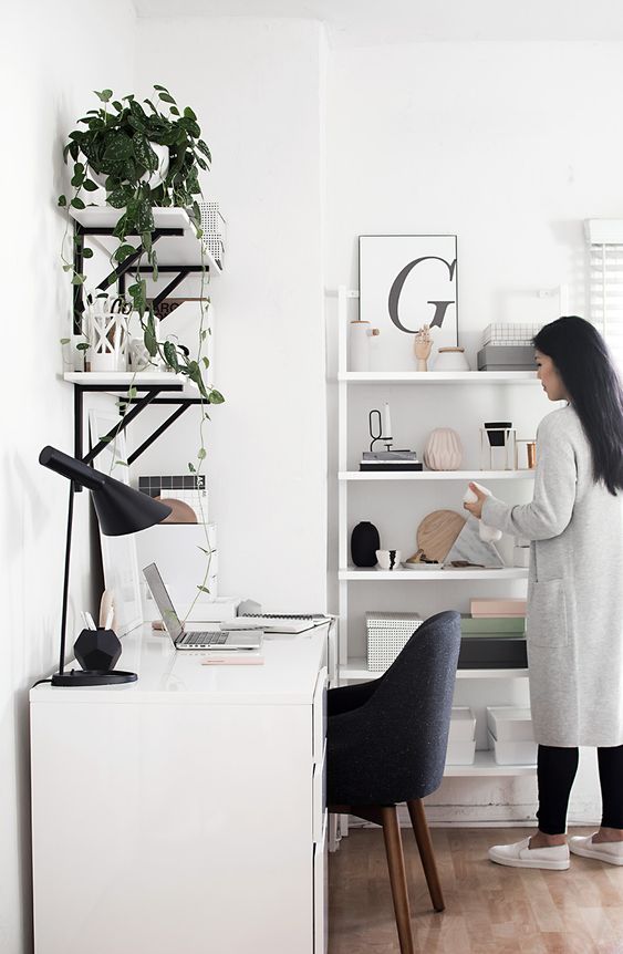 a stylish contemporary home office in white, with a black chair, lamp, black and white shelves on the wall