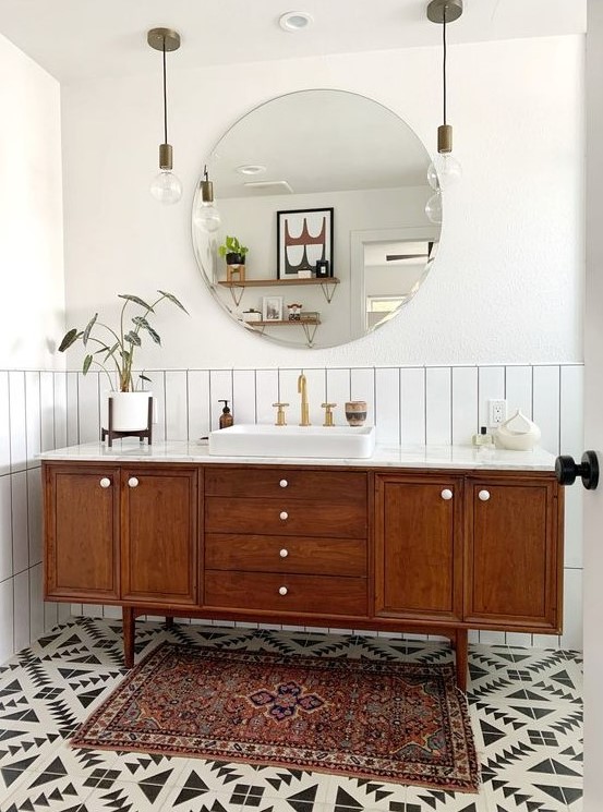 A stylish mid century modern bathroom with white skinny tiles, geo tiles on the floor, a boho rug, a wooden vanity and pendant lamps