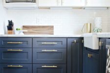 a trendy two tone navy and white kitchen with white countertops and gold hardware that give it a more modern feel