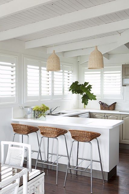 a tropial kitchen in grey and white, with wicker lampshades, wicker stools, grey cabinets and tropical plants