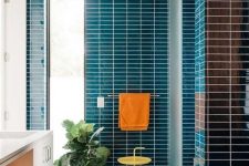 a vibrant mid-century modern bathroom clad with navy skinny tiles, a white flaoting vanity and touches of orange