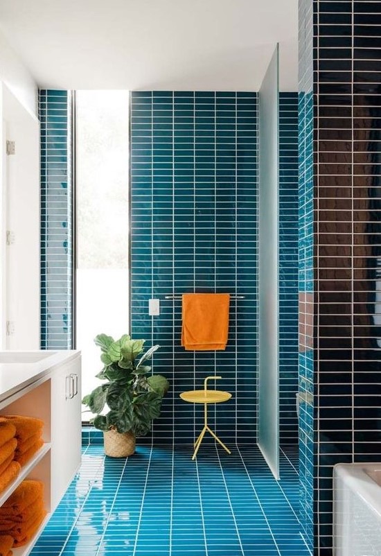 A vibrant mid century modern bathroom clad with navy skinny tiles, a white flaoting vanity and touches of orange