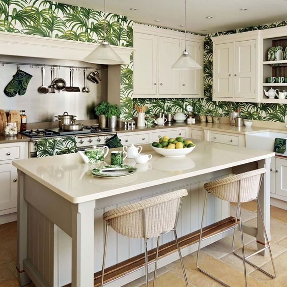A vintage inspired tropical kitchen with creamy cabinets and tropical leaf wallpaper wall over plus wicker stools