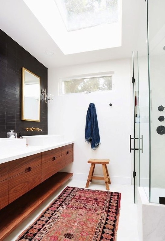 a welcoming mid-century modern bathroom with black and white tiles, a shower space, a double stained vanity, metallic fixtures