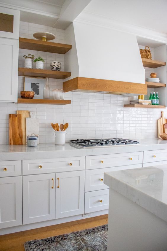 A welcoming white kitchen with shaker cabinets, stone countertops, a white skinny tile backsplash and light stained wooden touches