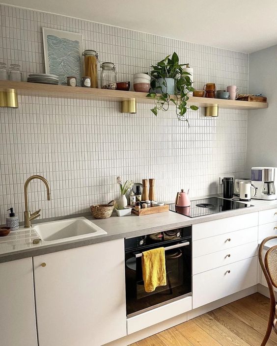 a white Scandinavian kitchen with an off-white skinny tile backsplash, stone countertops and an open shelf with dishes and decor