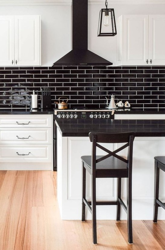 a white farmhouse kitchen with black glossy tiles, a black hood and countertops plus black stools