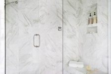 a white marble shower with a floating bench and a mosaic floor is a stylish and refined idea