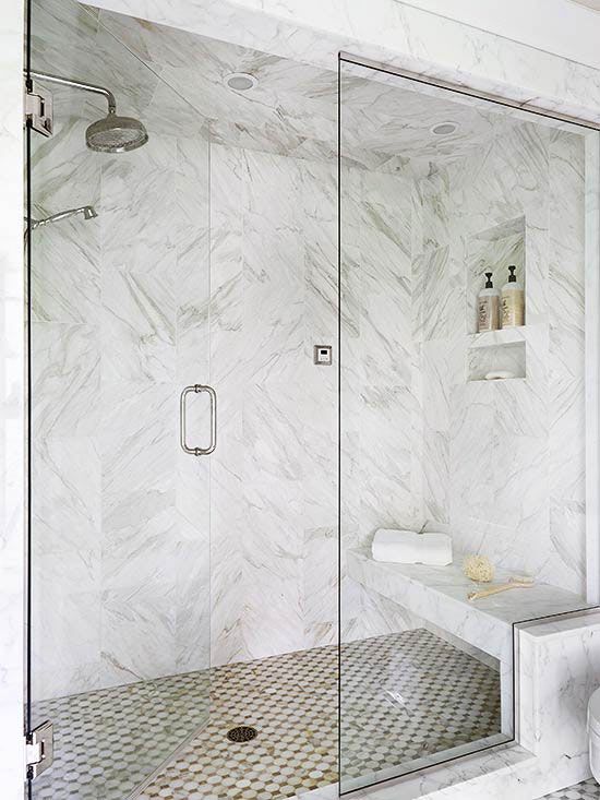 a white marble shower with a floating bench and a mosaic floor is a stylish and refined idea