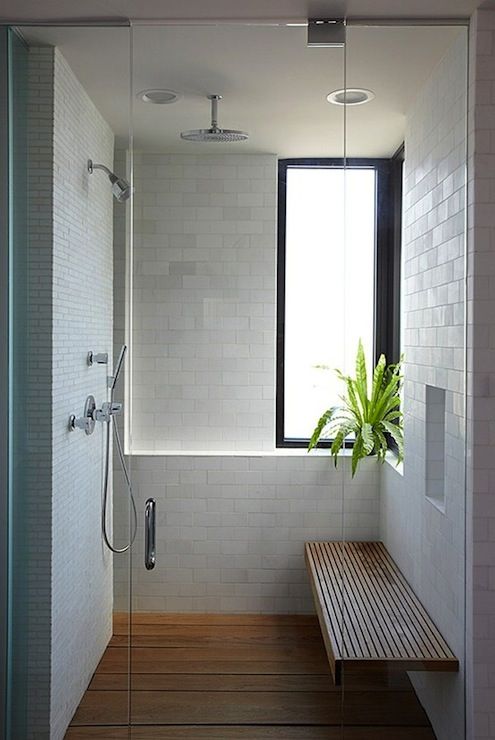 a white shower space with a frosted glass window, a floating wooden bench and a matching floor plus a potted plant