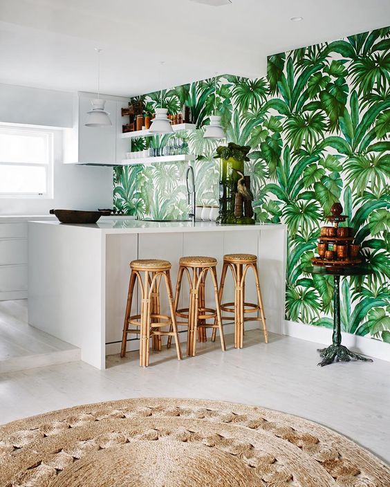 a white tropical kitchen with a tropical leaf print wall, rattan stools, a jute rug feels contemporary and boho