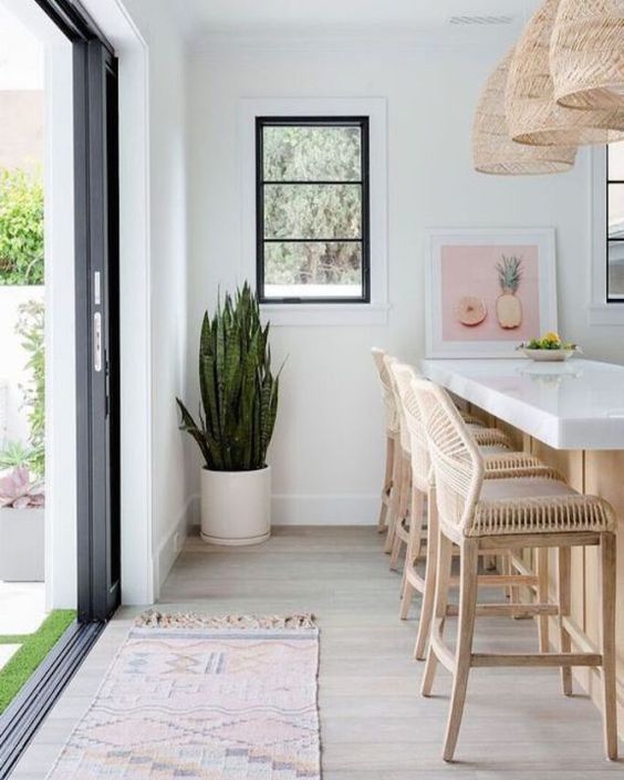 a white tropical kitchen with rattan stools, wicker pendant lamps plus a tropical plant in a pot