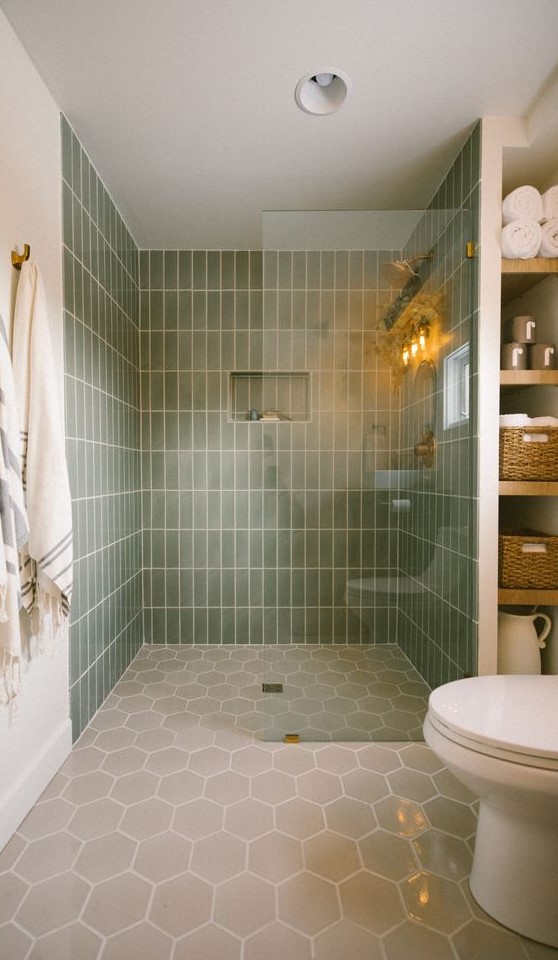 An earthy bathroom with skinny green and grey hexagon tiles, a large shower space, built in shelves and white appliances