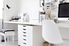 an eclectic black and white home office with white furniture, a black lamp, frames for artworks and a stool with a striped seat