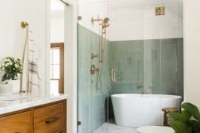 an elegant mid-century modern bathroom with skinny green tiles, a shower and a tub, a mosaic tile floor, a stained vanity and a rug