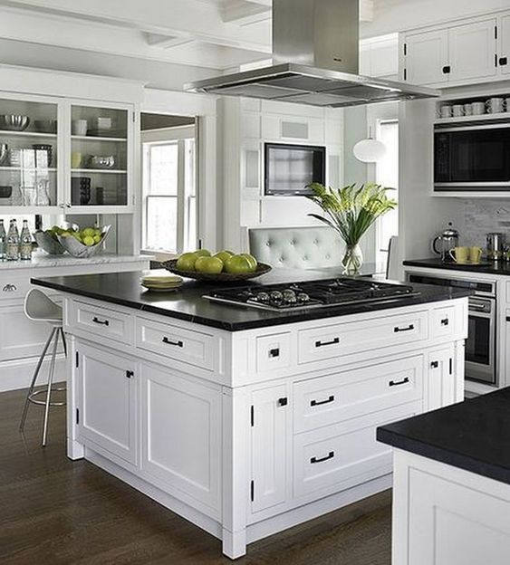 Vintage inspired white cabinets and a large kitchen island in the center with black countertops and black hardware