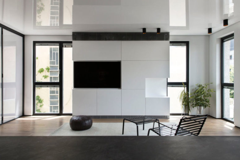 The living room is done with a sleek white TV cabinet and a built-in TV, a chair, a footrest and a leather ottoman