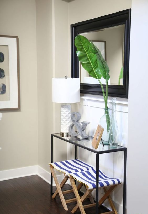 tropical leaves in a clear vase and striped nautical folding stools under the console add a slight beachy feel