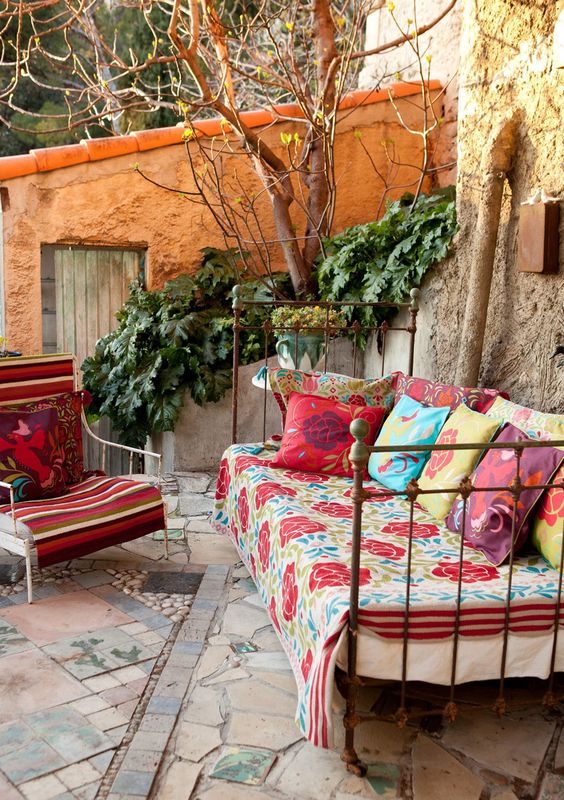 a shabby chic metal daybed with colorful blankets and pillows for a gypsy boho outdoor space