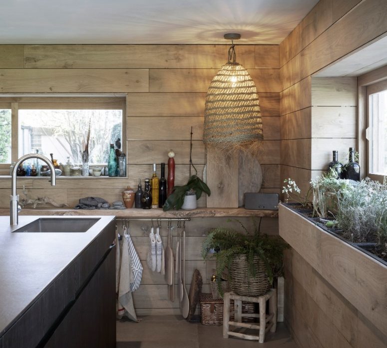 The kitchen is clad with light-colored wood, a wicker lamp, a basket planter and a metal kitchen island