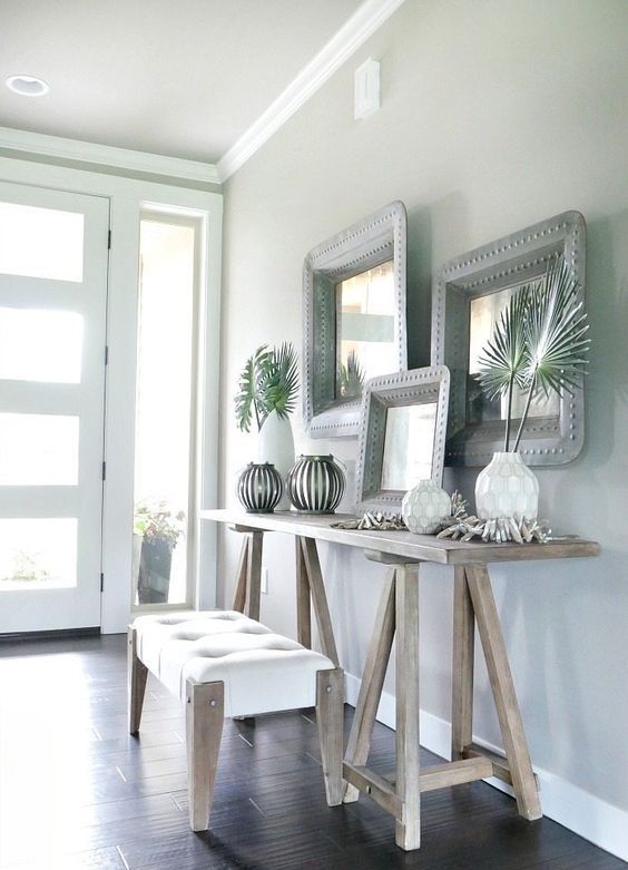 a neutral tropical entryway with light-colored wooden furniture, vases with tropical leaves, driftwood and mirrors in metal frames