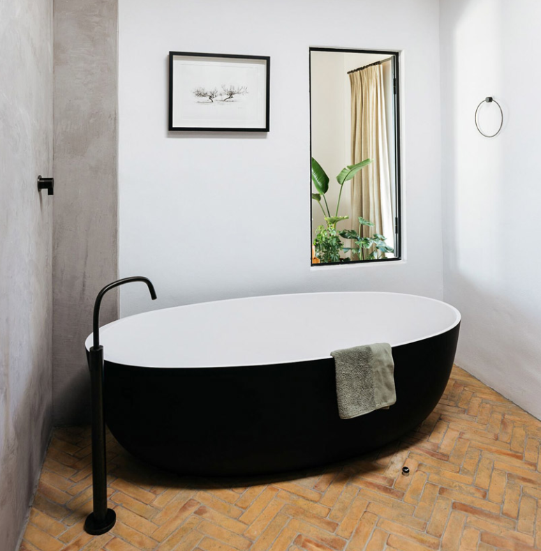 The bathroom is done with a black and white bathtub a black faucet and a large mirror