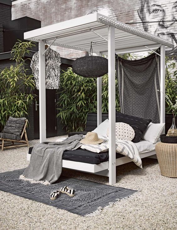 A cabana style wooden daybed with a hanging blakc lamp, a curtain and lot sof pillows and blankets welcomes with its look