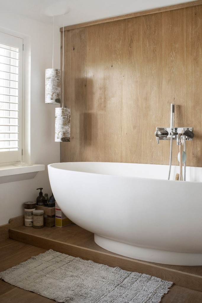 The bathroom is done with light colored wood and a modern oval tub