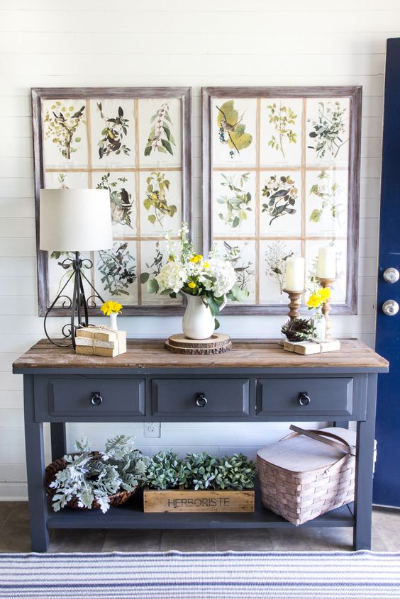 a farmhouse console table with greenery in crates and baskets and vintage botanical posters as artworks