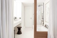 09 The bbathroom is also white, with a tub, a marble floating vanity, a wooden door and some curtains for privacy