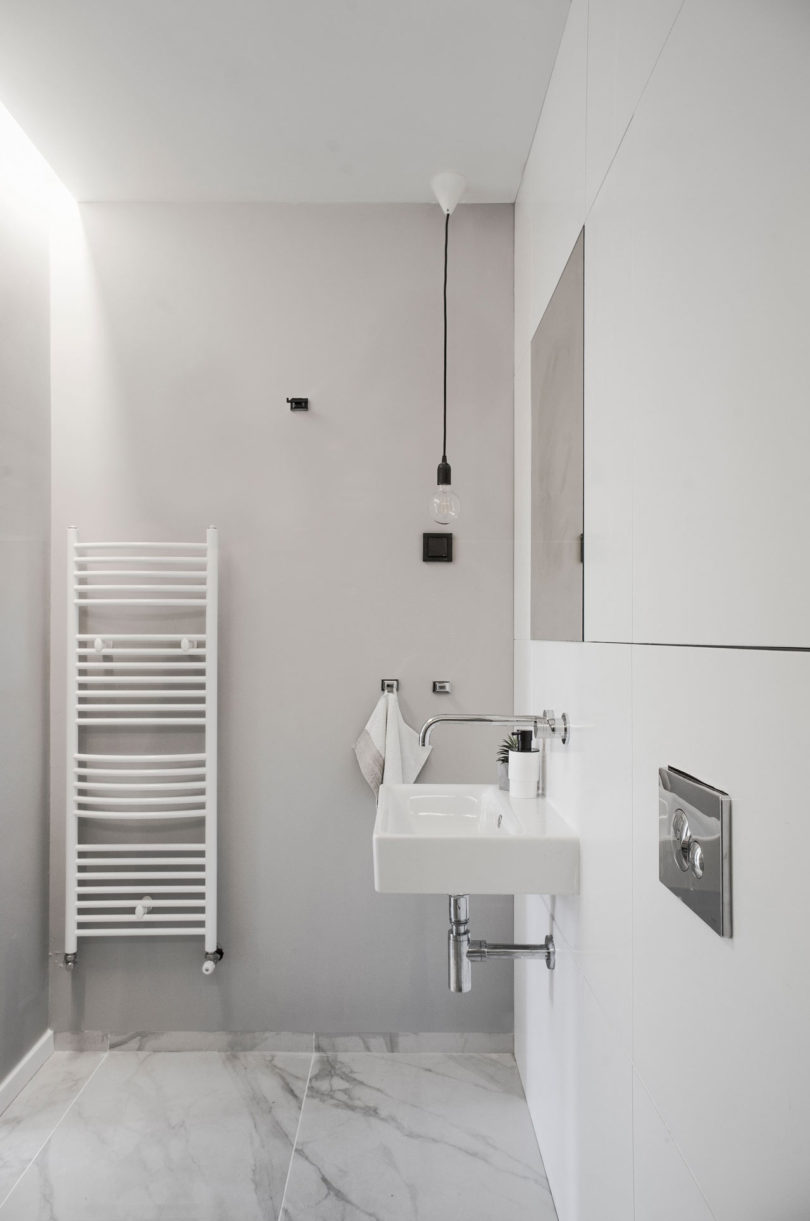The bathroom is minimalist, with white marble tiles and bulbs plus a wall mounted sink