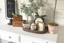 10 a cozy summer farmhouse entryway with a sign, pale greenery, a basket, some pots and porcelain