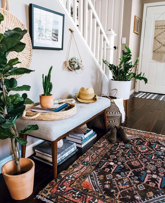 a boho summer entryway with potted plants and cacti, a boho rug, a wicker basket and an artwork