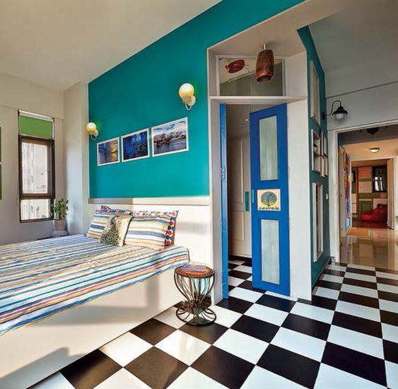 a retro bedroom with a black and white tile floor, a teal wall and a bright blue door for more color