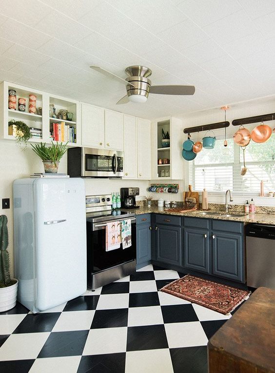 A retro kitchen with a black and white tile floor, colorful pots and pans and a retro inspired pastel fridge