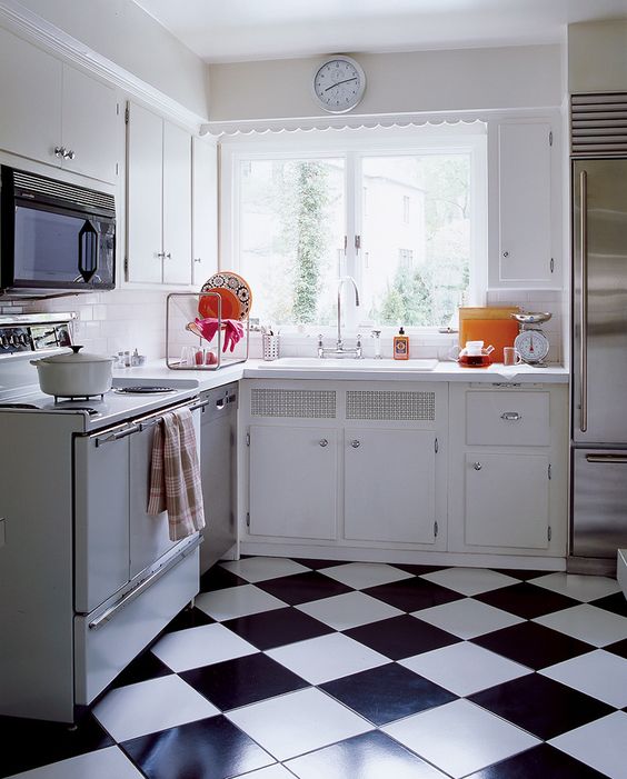 a 1950s inspired kitchen with a black and white tile floor and neutral cabinets yet colorful plates and pots
