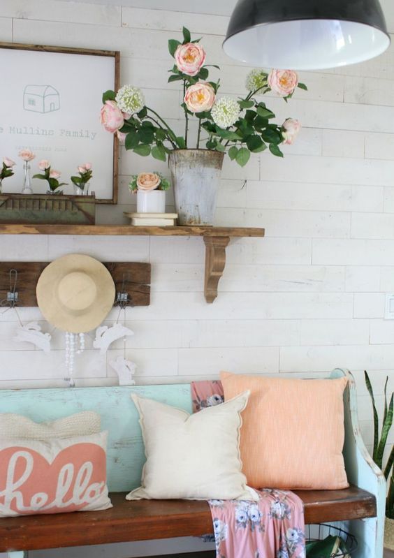 A bright vintage inspired summer entryway with coral blooms in a vase and tubes, coral pillows, a straw hat and a blue bench