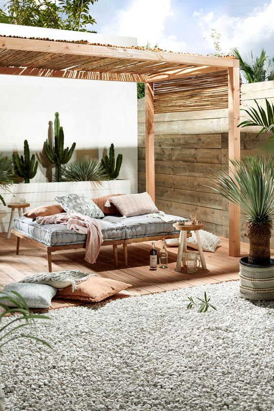 a simple and welcoming wooden daybed with a comfy mattress and pillow placed in a cabana to avoid sunlight