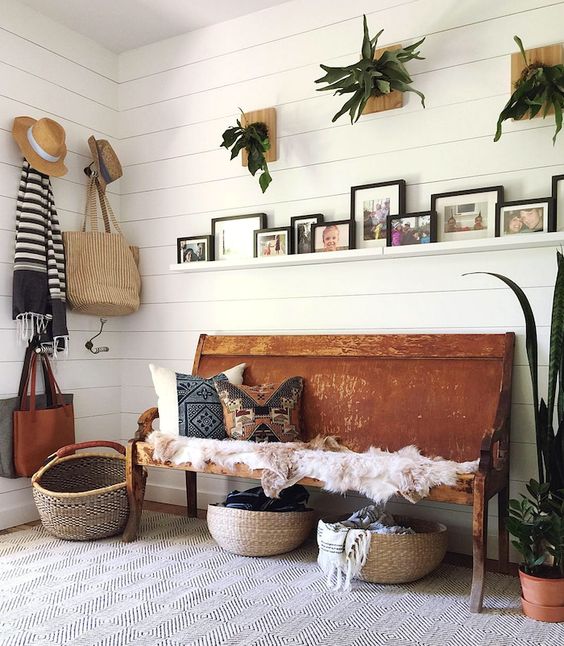 a summer boho entryway with potted greenery, a bench with printed pillows, baskets for storage and wicker elements