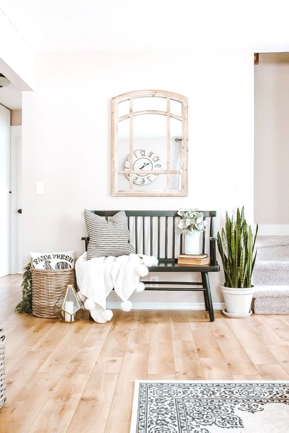 a summer farmhouse entryway with a succulent in a pot, a basket with greenery, a candle lantern, a bench and a pompom blanket