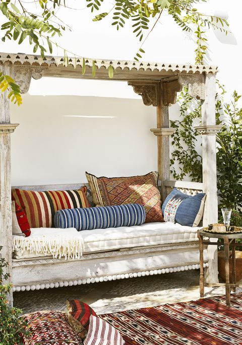 a whitewashed wooden daybed with a roof over it and lot sof colorful pillows is a gorgeous boho place to have a siesta