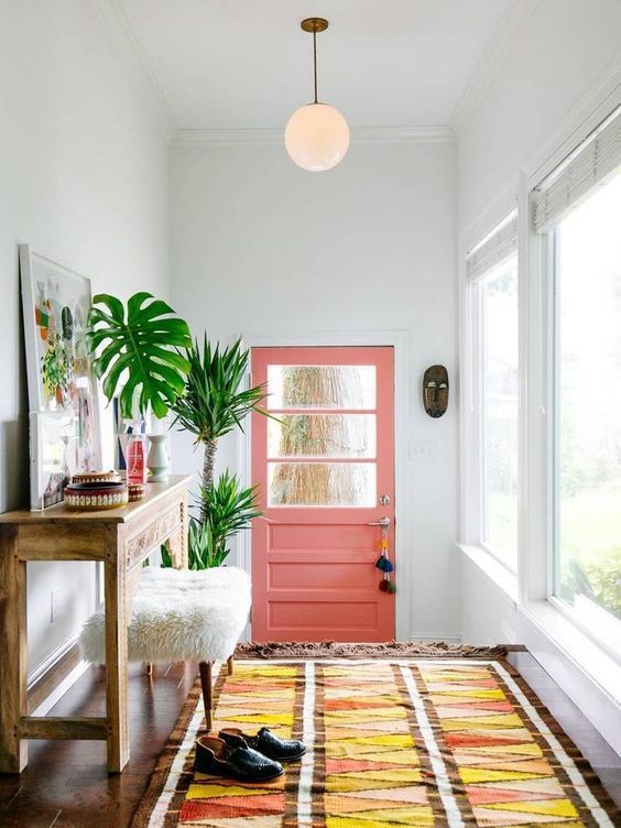 summer vibes are achieved with a pink door, a bright boho rug, potted palms and a bold artwork