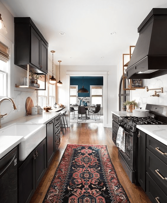a black galley kitchen with white stone countertops and elegant brass touches here and there