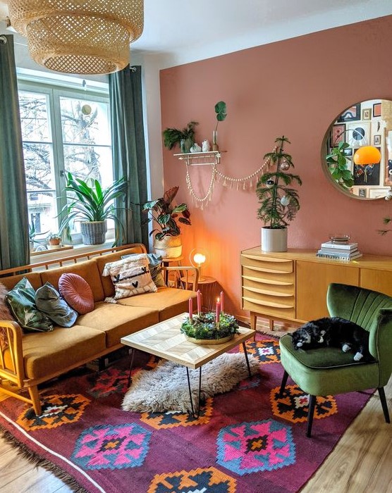 a bold eclectic living room with a muave accent wall, an orange sofa, a bold rug, a coffee table, a stained dresser, green curtains, potted plants