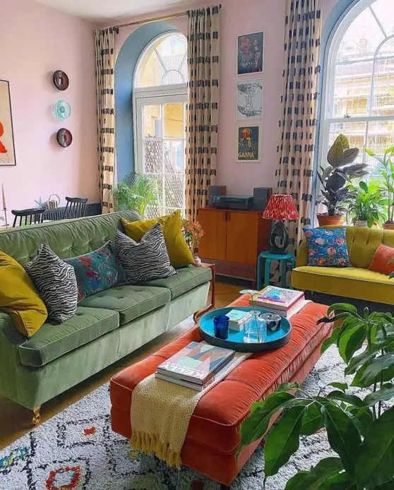 A vibrant eclectic living room featuring pink walls, a green sofa, a neon yellow loveseat, and an orange ottoman. Potted plants and bright artwork add life to the space. This mix of colors and styles creates a lively and dynamic atmosphere.