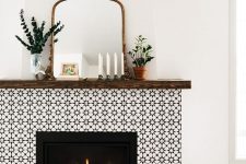 a bold fireplace clad with black and white prnted tiles, with a dark mantel, greenery, a mirror in a vintage frame and candles