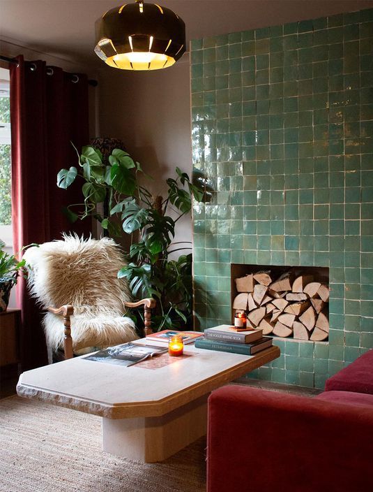 A bold living room with a non working fireplace surrounded with green Zellige tiles, with firewood inside